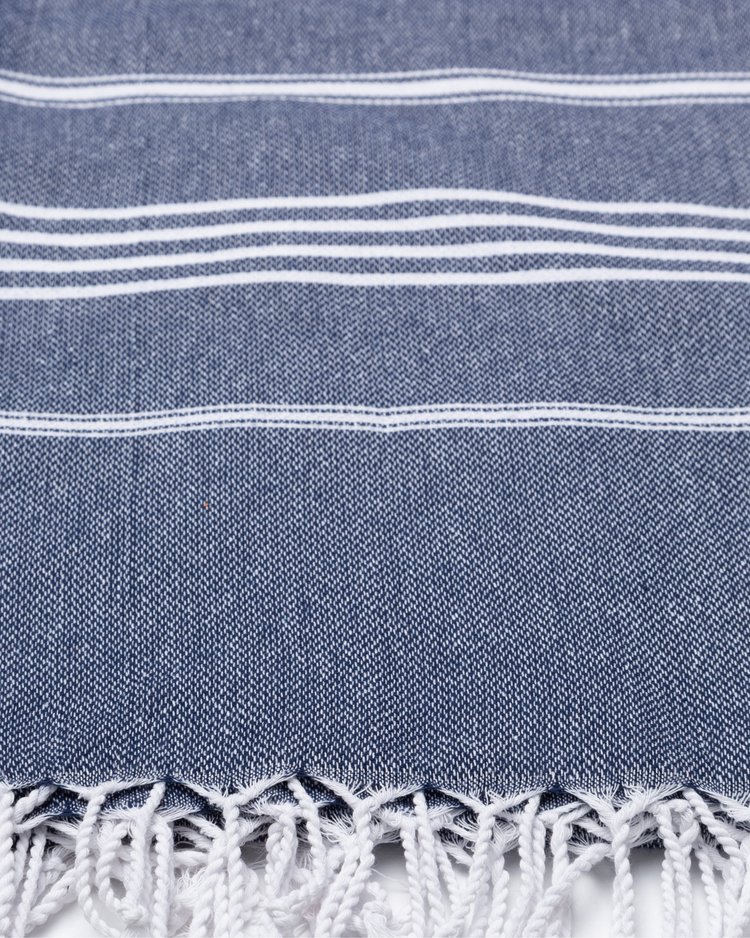 Mörkblå bomullshammamhandduk med vita ränder och fransar i nederkant.