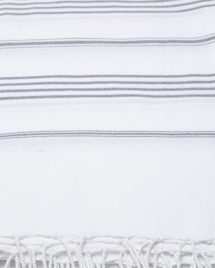 Vit bomullshandduk med grå ränder och fransar i traditionell hammamstil.