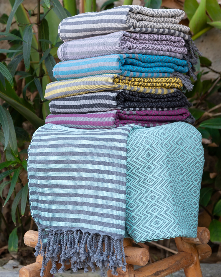 Turkisk hammam handduk i körsbärsröd och blå med mönster och fransar, vikta i stapel.