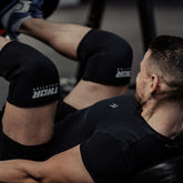 Svart neopren knäskydd 7mm med vitt tryck, flexibelt stöd för träning och sport.