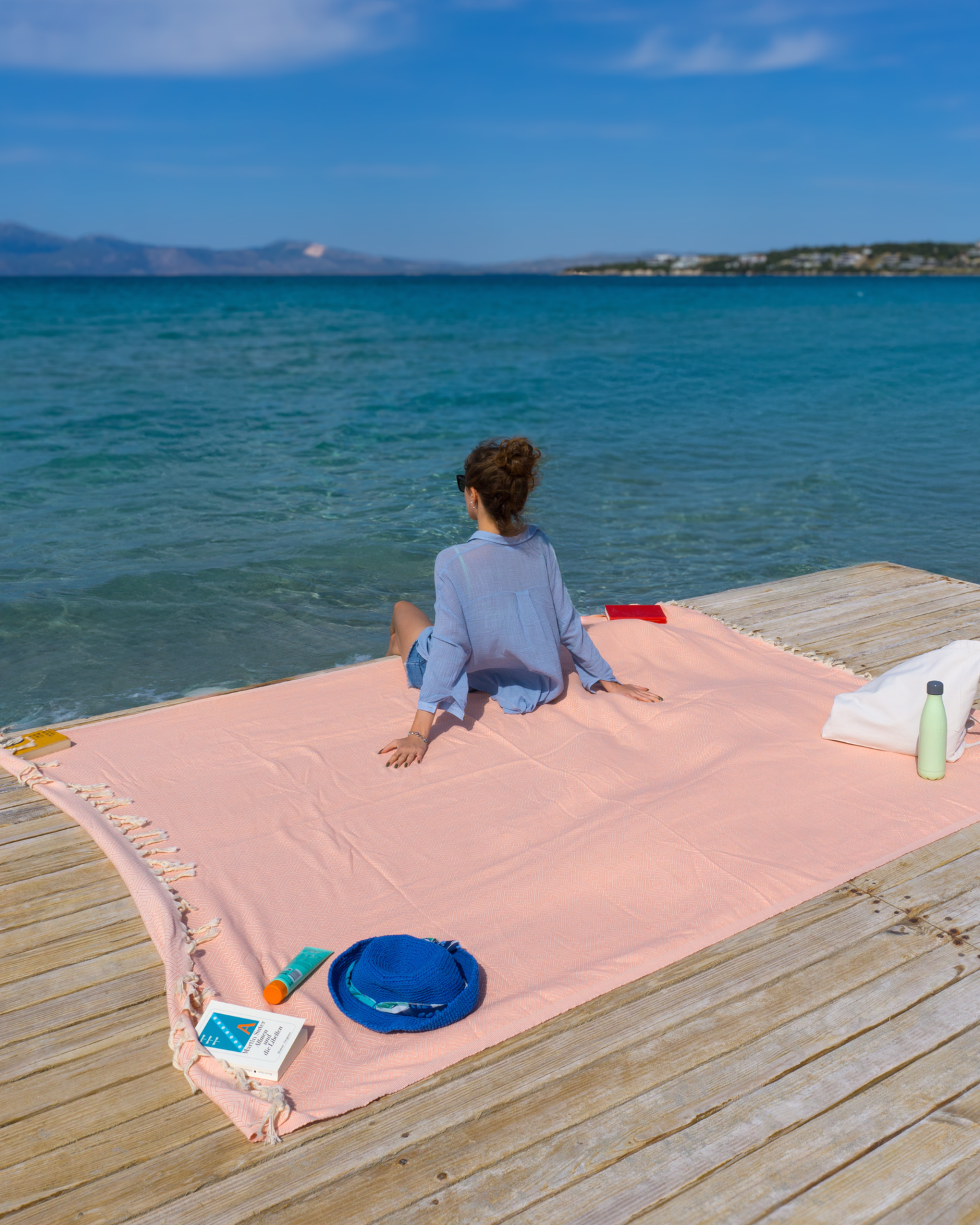 Salmonfärgad XXL strandhandduk i mjuk bomull med fransar, bredvid strandprylar på träbrygga.