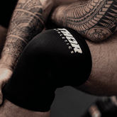 Svart neopren knäskydd med vit logotyp, elastiskt och stödfunktion för träning och sport.