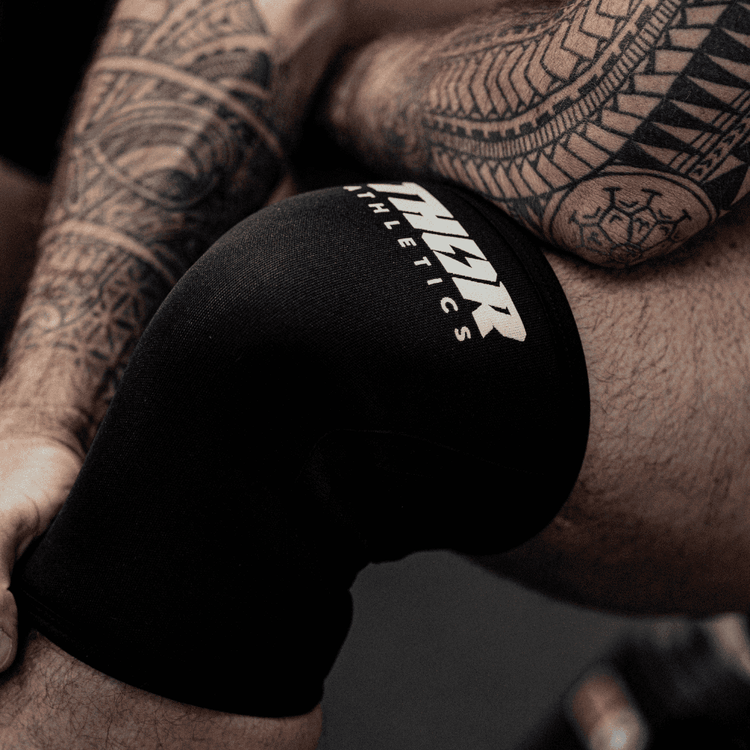 Svart neopren knäskydd med vit logotyp, elastiskt och stödfunktion för träning och sport.