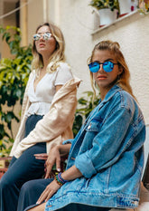 Runda solglasögon med spegelglas och tunn svart båge, bärs av kvinna i jeansjacka.