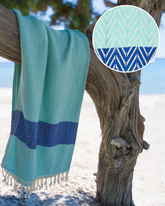 Mintblå bomullshandduk med mörkblå geometriska ränder och fransar, snabbtorkande och sandavvisande.