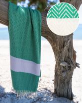 Grön och vit hammam-handduk med fiskbensmönster och fransar, hängande på trädstam.