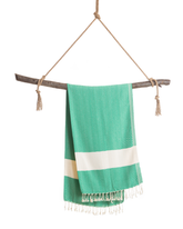 Grönvit pestemal handduk med vit rand och fransar, hänger på rep och träpinne.