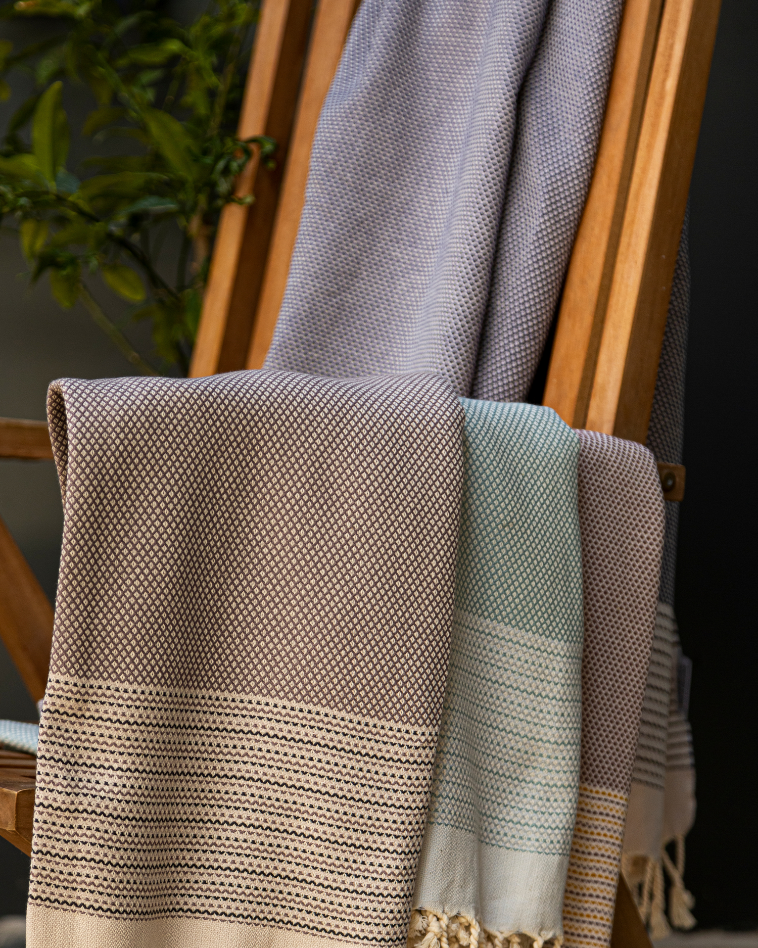 Mjuk turkisk hammamhåndduk i antracitgrå med vävd mönster och fransar, hängande på trästol.