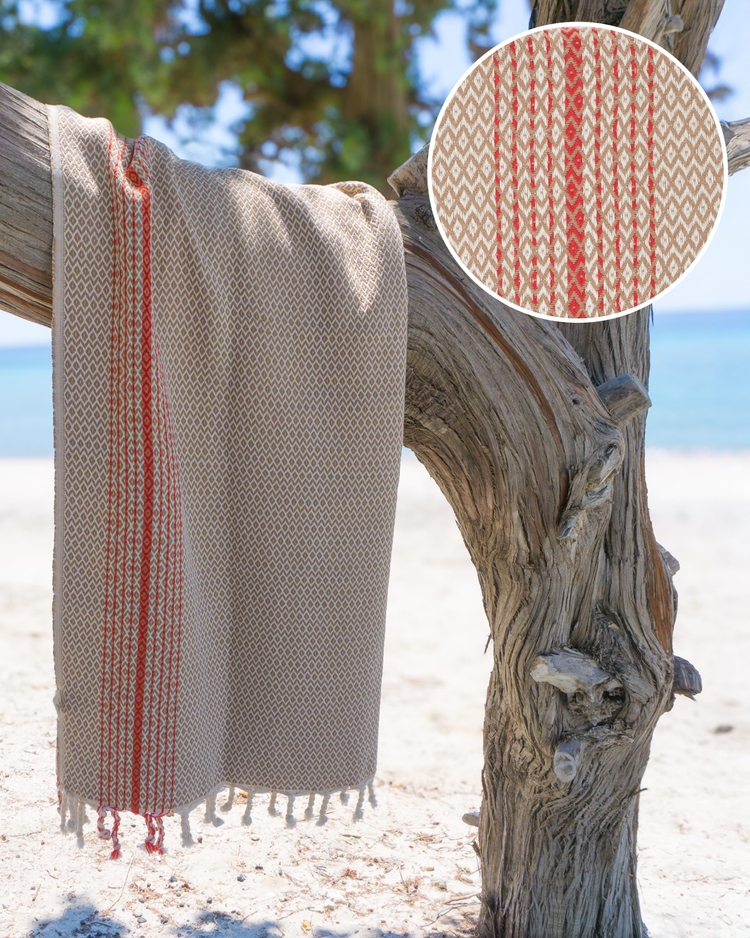Beige turkisk hammam handduk i bomull med röd mönstrad rand och fransar, hängande på träd.