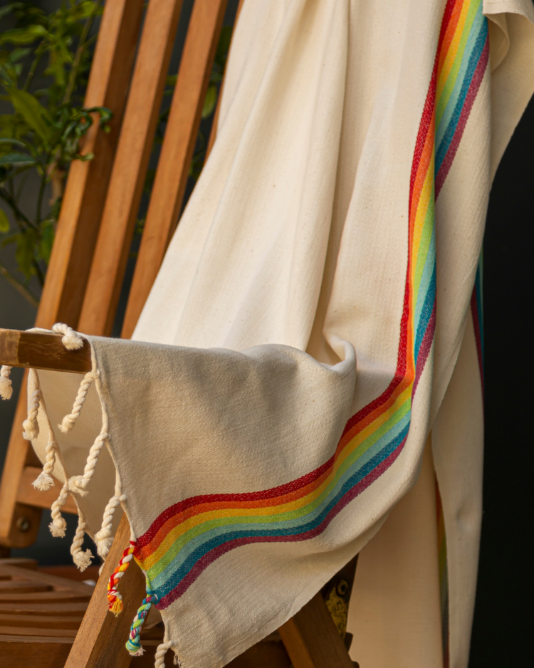 Beige bomullsstrandhandduk med regnbågsrand och tofsar, turkisk hammamstil.