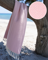 Ljusrosa hammam strandhandduk i mjuk turkisk bomull med dekorativa fransar, draperad över trägren.