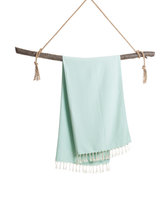 Mintgrön turkisk hammam handduk i bomull med fransar, hängande över träpinne.