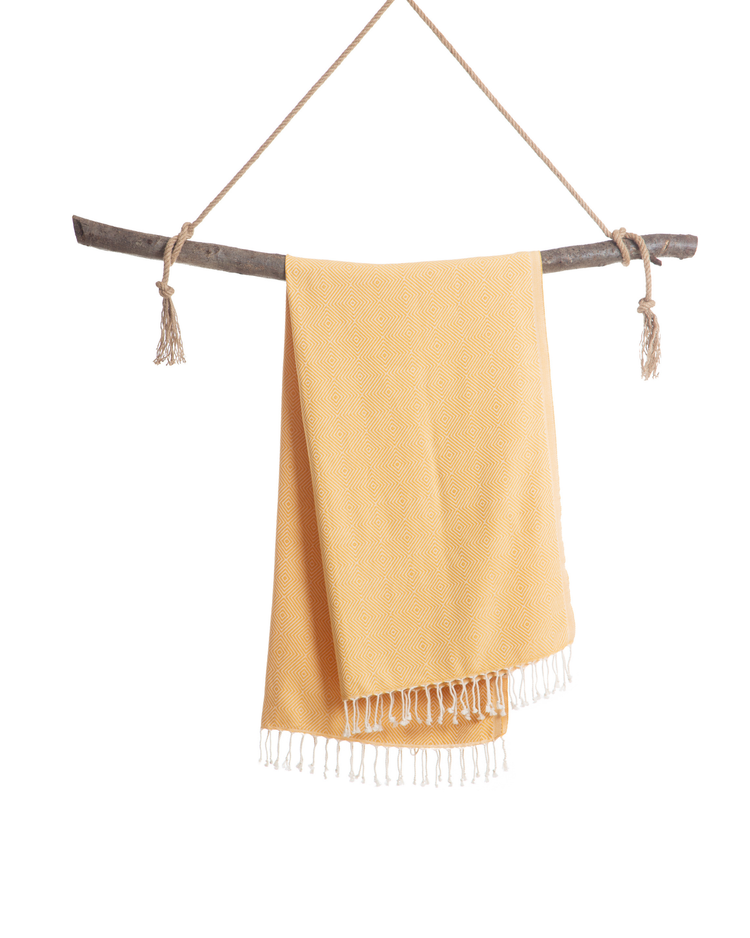 Gul turkisk hammamhandduk med fransar i bomull, hängande på träpinne.