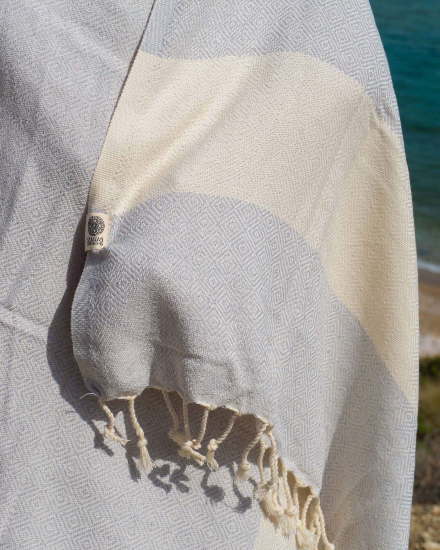 Grå och vit randig hammam strandhandduk med fransar och etikett, lätt och kompakt.