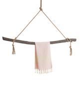 Ljusrosa hammamhandduk i tunn bomull med fransar, hängande över träpinne.