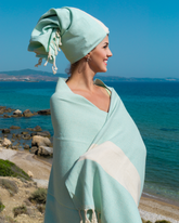 Mintfärgad hammam handduk i bomull med vita ränder och dekorativa fransar, använd som hår- och kroppshandduk.