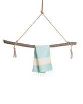 Mintfärgad hammam handduk med vita ränder och korta fransar, hängande på träpinne.