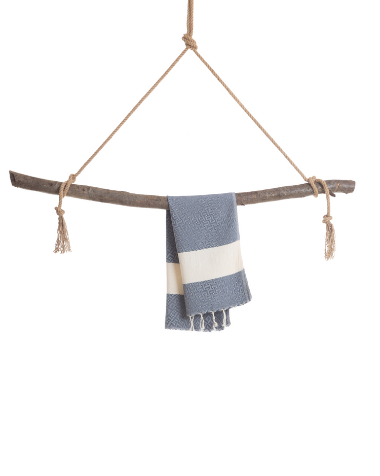 Blå och vitrandig hammam handduk med fransar, hängande på naturfärgat rep och träpinne.