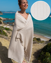 Beige hammam handduk i mjukt, lättvikt bomull med mönster och fransar, insvept runt kvinna vid havet.