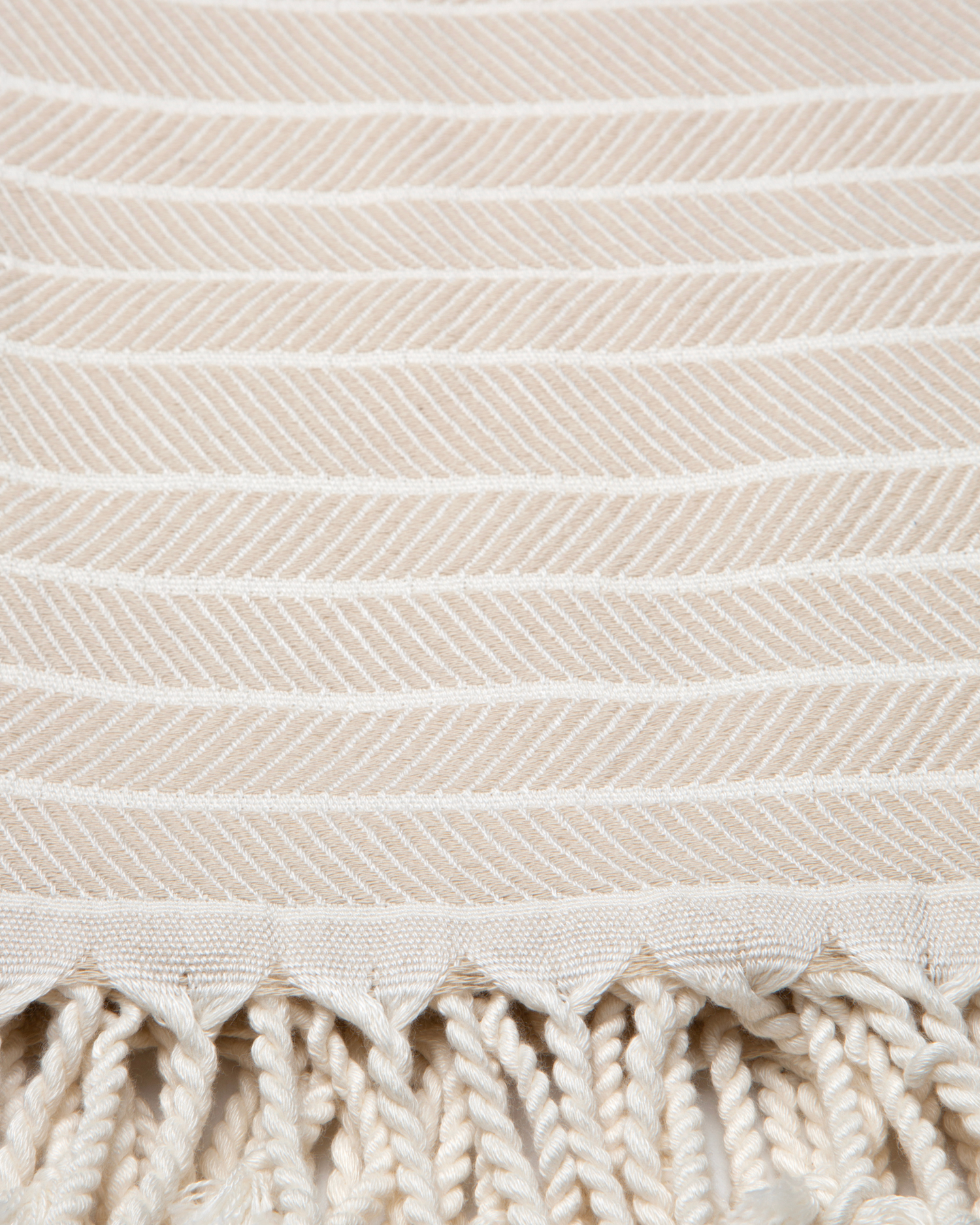 Beige turkisk hammam handduk i bomull och bambu med vitrandigt mönster och tofsar.