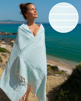 Mintgrön tunn hammamhandduk med vita ränder och fransar, draperad runt kvinna vid havet.