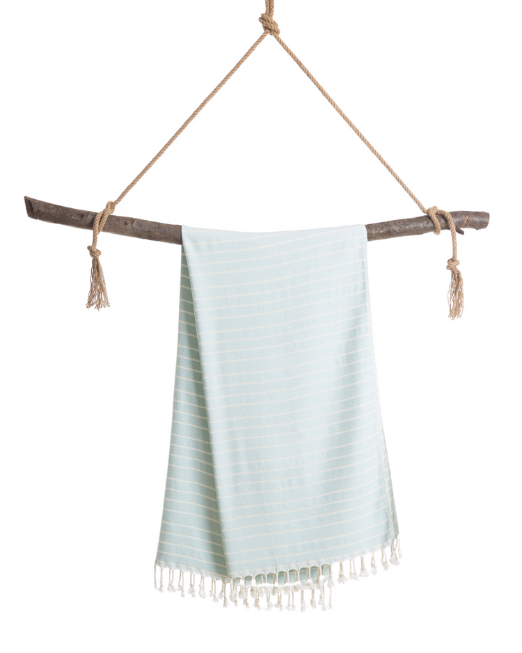 Mintgrön turkisk hammamhandduk i bomull och bambu med vita ränder och fransar, hängande på träpinne.