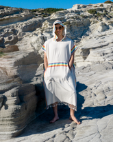 Vit strandponcho med huva och regnbågsmönstrade kanter i bomull och bambu, med fransar nedtill.