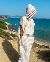 Randig svartvit bomullsstrandponcho med huva och ficka, på klippa vid havet.