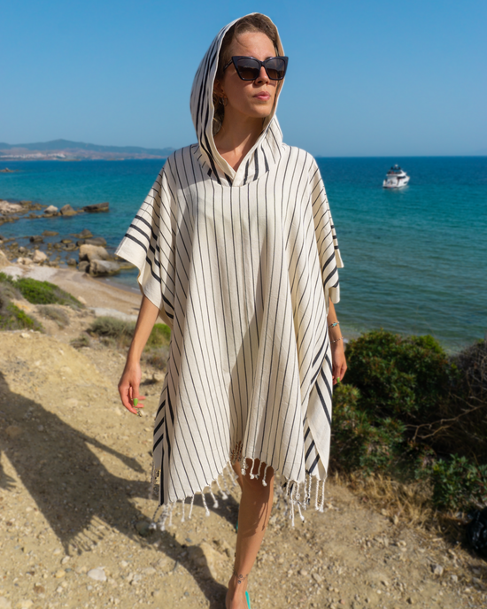 Randig svart och vit damhooded strandponcho i lätt bomull med fransar, bärs vid havet.