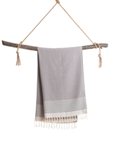 Anthracitfärgad turkisk hammamhanduk med fransar, hängande på trädgren.