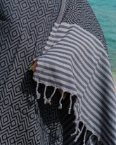 Svart hammam handduk med diamantmönster och gråvit randig hammam strandhandduk med fransar.