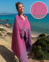 Körsbärsröd hammam handduk med blå randmönster och fransar, insvept runt kvinna vid havet.