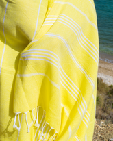 Gul peshtemal strandhandduk med vita ränder och fransar, lätt bomullstyg.