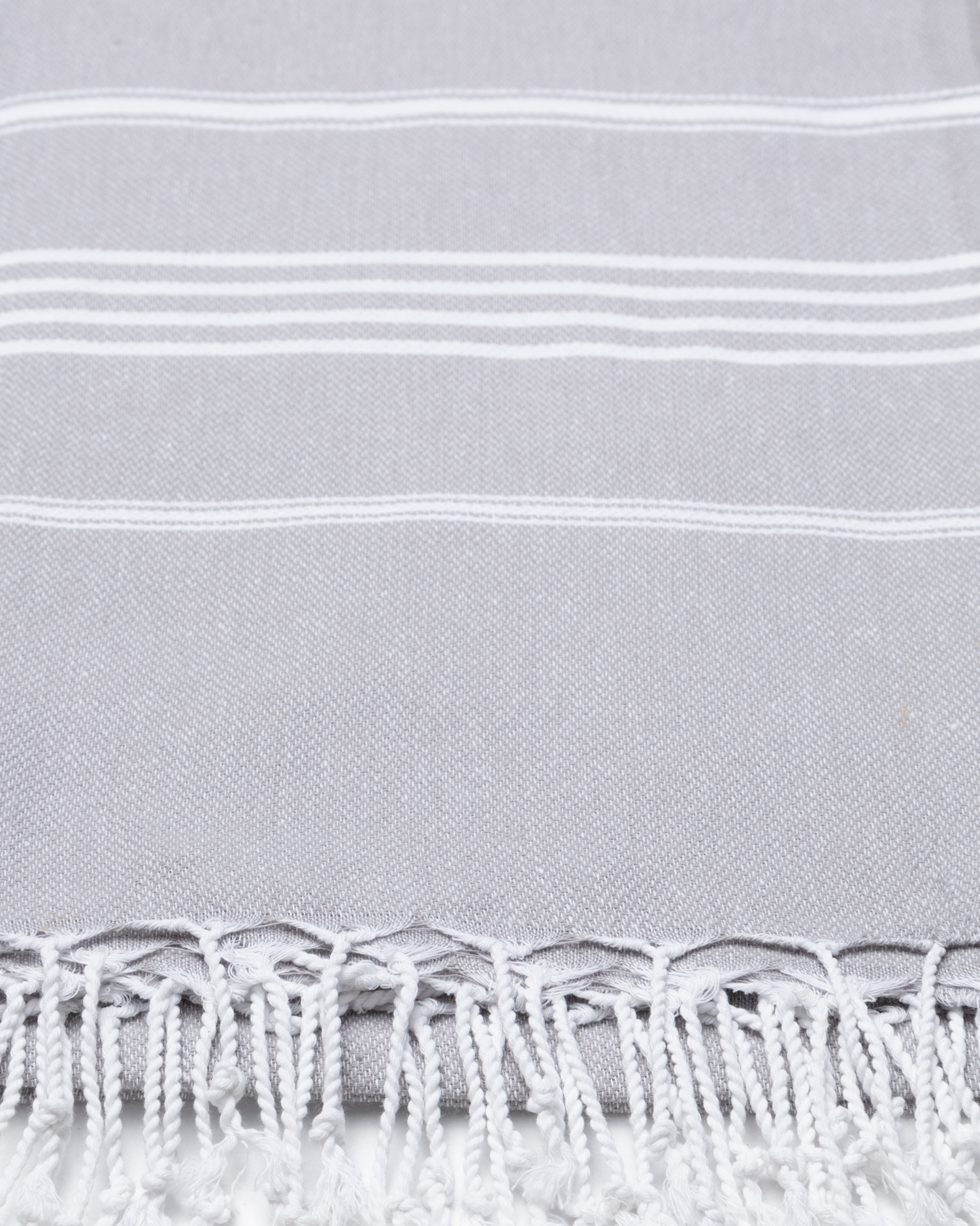 Grå bomullsstrandhandduk med vitrandigt mönster och fransar i turkisk hammamstil.