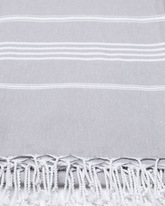 Grå bomullsstrandhandduk med vitrandigt mönster och fransar i turkisk hammamstil.