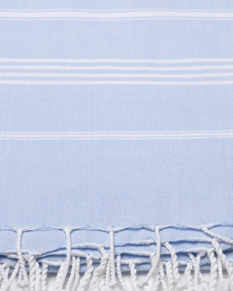 Ljusblå bomullshandduk med vita ränder och fransar, lätt och kompakt peshtemal-textur.