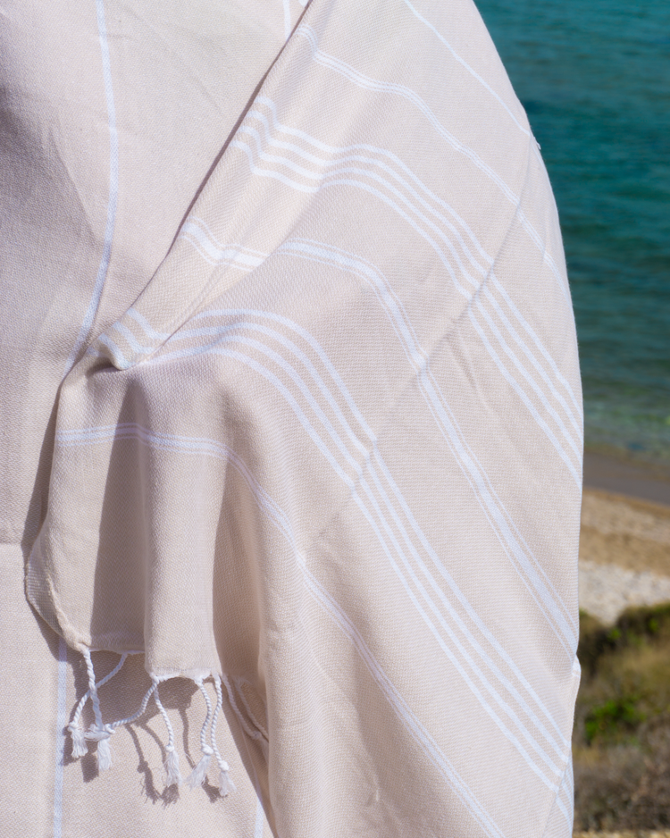 Beige randig bomullshandduk med fransar, lätt och kompakt design, hammam-stil.