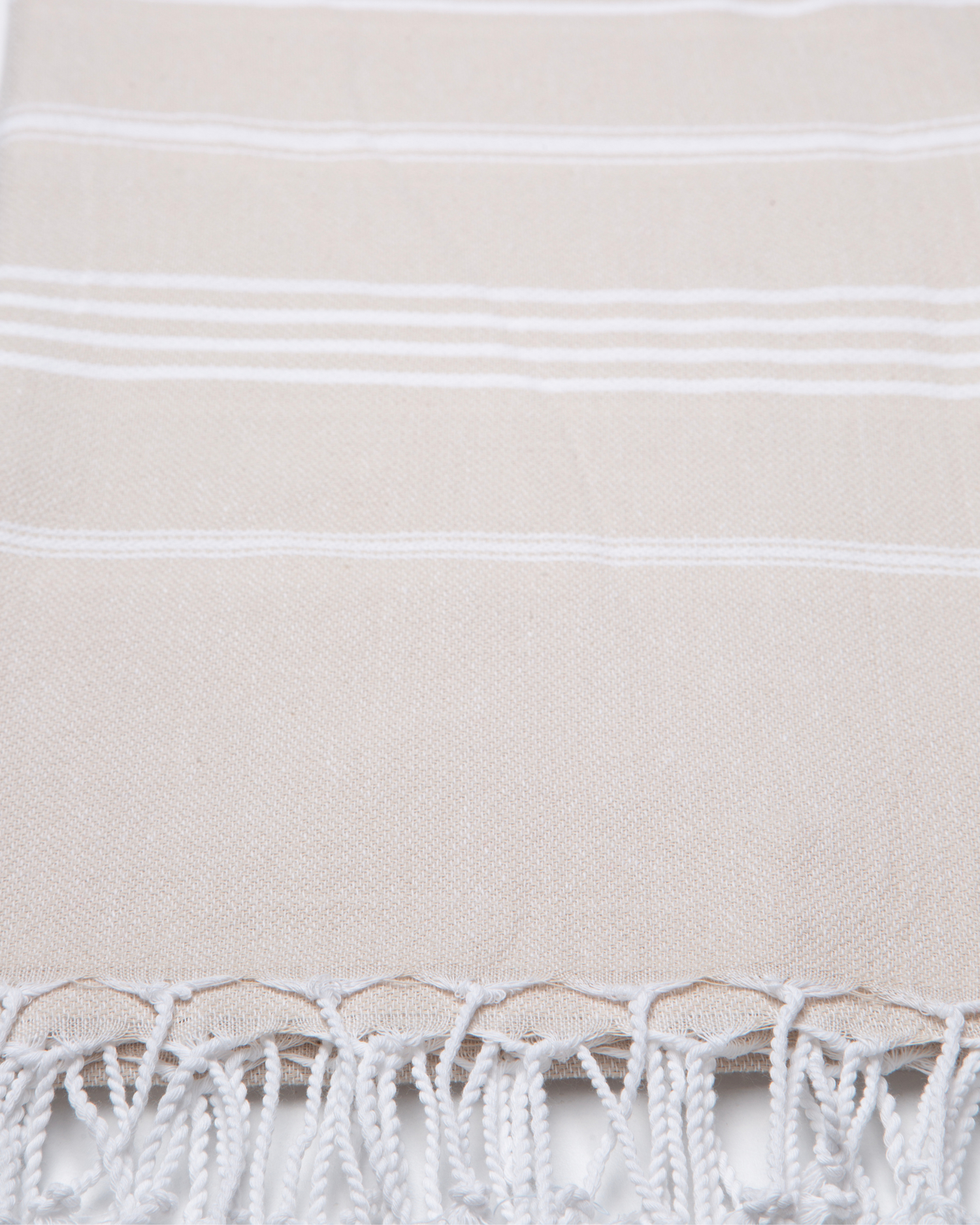 Beige bomullshandduk med vita ränder och fransar, lätt och kompakt design.