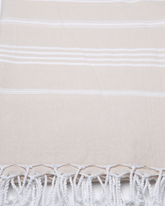 Beige bomullshandduk med vita ränder och fransar, lätt och kompakt design.