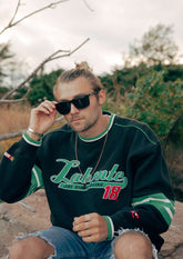 Svarta wayfarer-solglasögon med aluminiumram och tjocka stänger på man i casual sweatshirt utomhus.