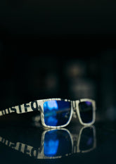 Fyrkantiga solglasögon i återvinningsbart papper med blåa spegelglas och vit svarta detaljer.