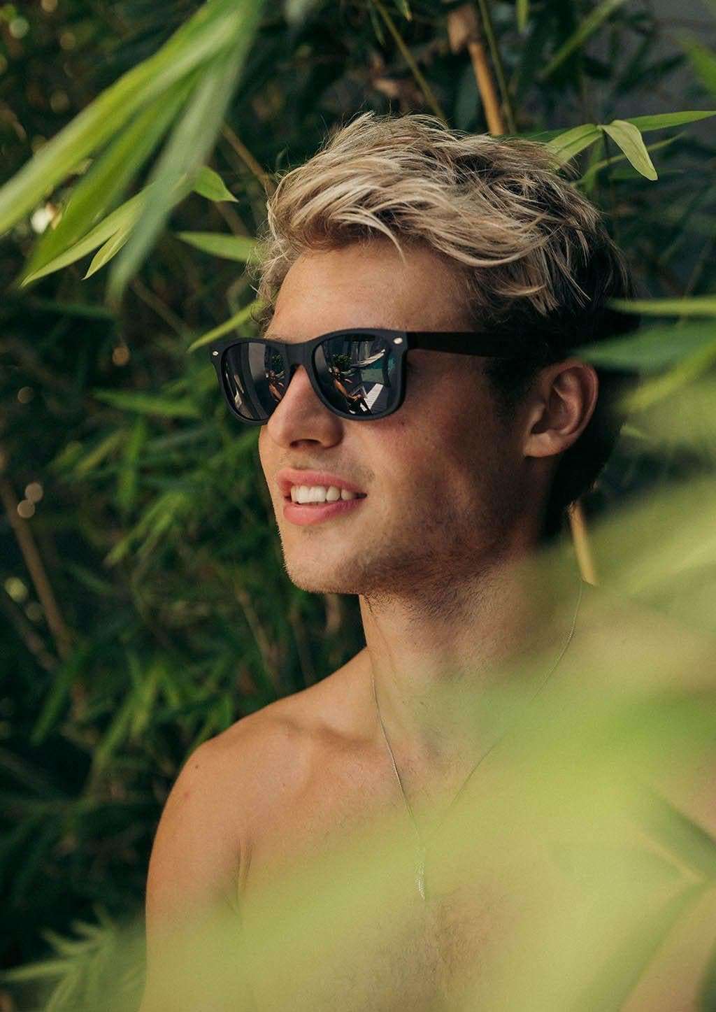 Svarta Wayfarer-solglasögon med rosenträbågar och polariserade linser på person utomhus.