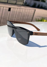 Solglasögon med svart fyrkantig ram och bruna träbågar med unik träådring, polariserade linser.
